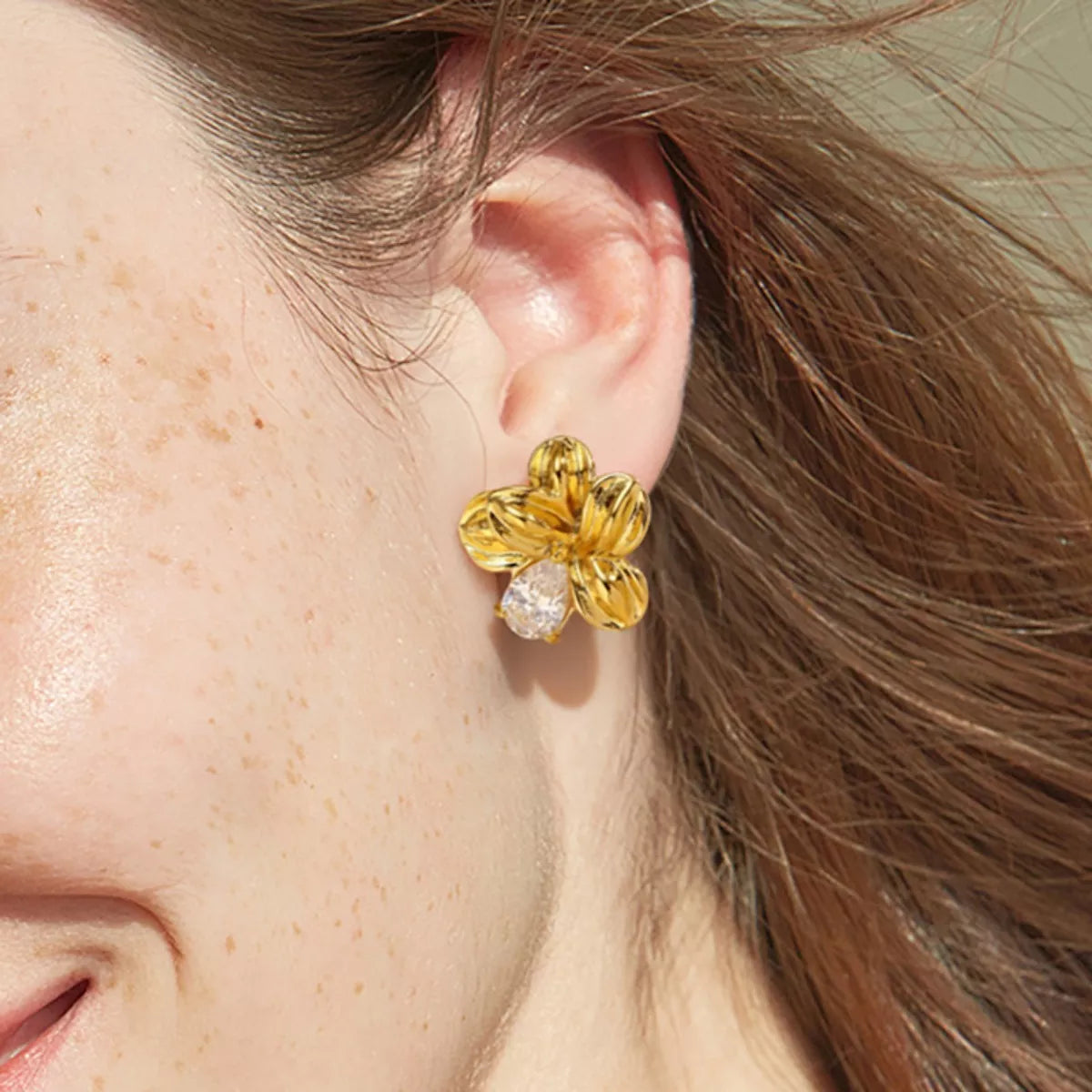  "Woman wearing 18K gold-plated flower stud earrings, close-up side view"