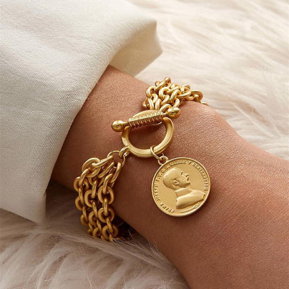 "Gold charm chain bracelet with portrait coin pendant on wrist"