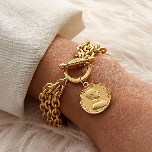 "Gold charm chain bracelet with portrait coin pendant on wrist"